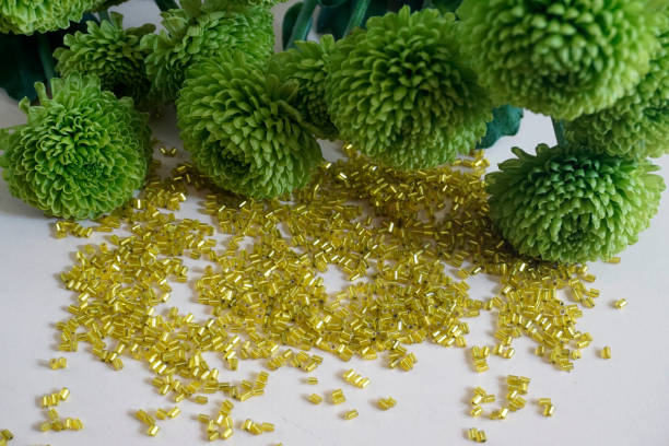 желтые трубчатые бусины тохо и зеленая хризантема на светло-кремовом фоне. - glass jewelry bead bugle стоковые фото и изображения