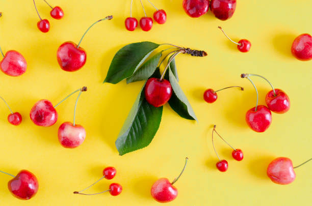 istock Red cherries on yellow background with leaves. Flat lay. 1205780616