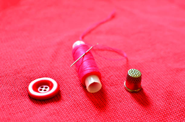 istock Accessories for sewing and darning clothes: needle, thread, buttons and thimble on a red background of wool fabric 1205782206