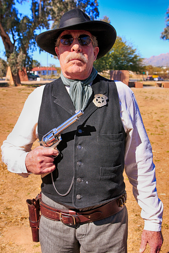 Close up of a re-enactor wearing a US Marshal tin star pinned to his black vest and holding his Colt Peacemaker revolver at the Cavalry day event at Fort Lowell Tucson AZ