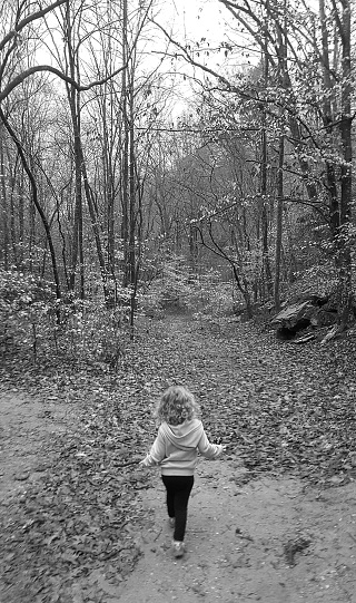 Girl walking confidently into forest on path. Black & white.