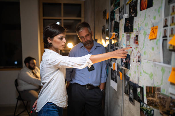 Police detective showing criminal's location to colleague on map attached to a wall Police detective showing criminal's location to colleague on map attached to a wall detective wall stock pictures, royalty-free photos & images