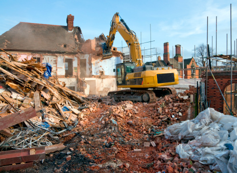 A large tracked excavator machine fitted with a demolition tool, ripping apart old houses and buildings in a town centre for re-development.