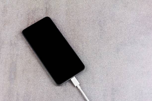 istock new smartphone with a black screen with a white wire from the charger on a gray background a close up view from the top with a copy space 1205795665