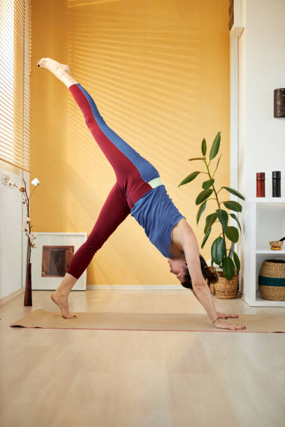 istock Attractive fit caucasian middle aged brunette doing Three Legged Downward-Facing Dog yoga pose in the morning. Home interior. 1205796907