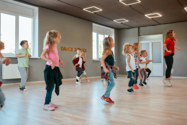 istock Repeat after me. Group of active children dancing in front of the large mirror while having choreography class in the dance studio. Female dance teacher and kids 1205805377