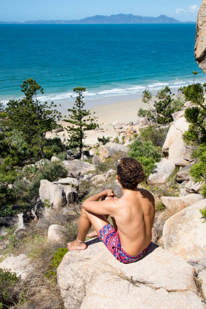istock Young man with hair bun and bathing suit, looking at ocean view 1205806205
