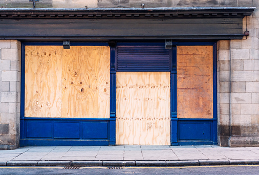 A traditional British shopfront, closed and boarded up with wooden boards.