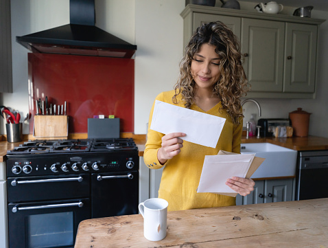 Young woman with curly hair drinking tea and checking her mail at home