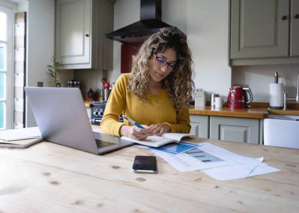 istock Beautiful young woman with curly hair working from home writing on notepad and using laptop and documents 1205813763