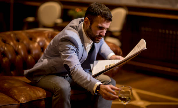 istock Young businessman drinking wine and reading newspaper in the office 1205817282