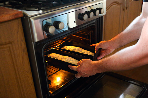 Man taking baked loafs of bread out of the oven. Baking bread at home. Close up