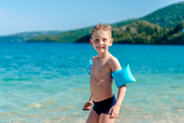 One boy is walking by the water on the beautiful beach. Smiling and looking at camera