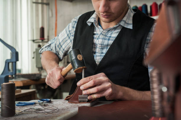 istock Close up of leather craftsman working with natural leather using hammer. 1205821515