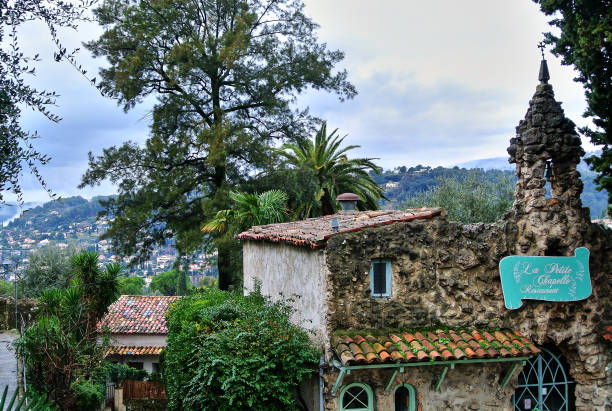 Saint-Paul-de-Vence / Provence - Alps - French Riviera, France - 02.14.2015: An ancient building made of stones with a tiled roof, inside is Le Restaurant de la Petite Chapelle, next to green bushes and trees.