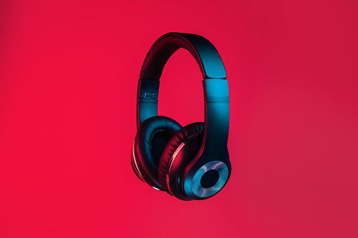 Retro 90s style photo of black stylish modern wireless headphone in neon lights over red background