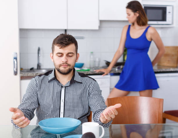 istock Young man sitting at kitchen table, woman preparing food 1205823669