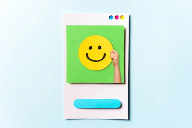 Photo of Concept of happy customer, employee, well done, feedback, opinion, social media. Hand showing a happy yellow smiling emoticon face on green and blue background with empty space for text.