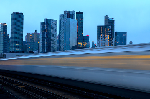 Motion blurred subway train against New York skyline at dusk, Queens, New York City.