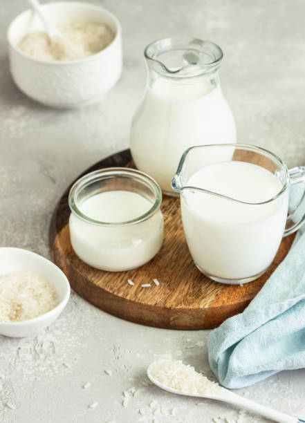 istock Rice milk in jugs and rice in a white ceramic bowls and spoon on a light grey stone background. Alternative type of milk. Vegan substitute dairy milk. 1205835452