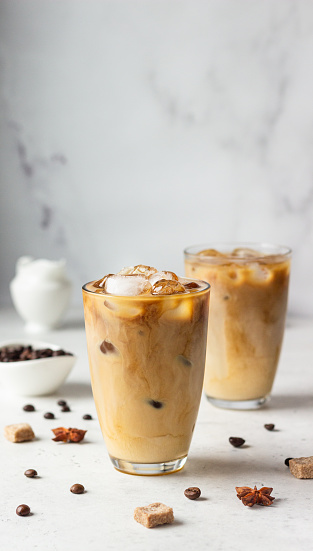 Cold brew coffee with spices and milk on light grey background. Spicy coffee with ice cubes.