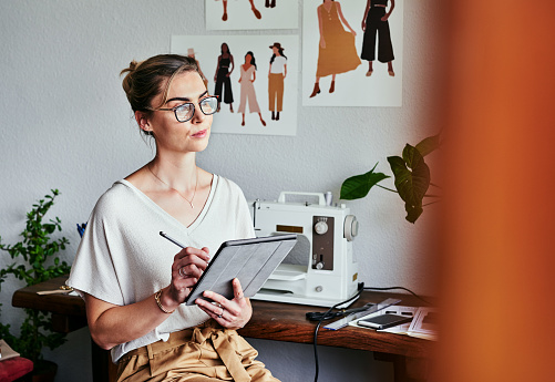 Cropped shot of a fashion designer using a digital tablet while sitting in her workshop