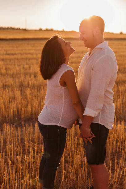 portrait outdoors of a young young pregnant couple in a yellow field. outdoors family lifestyle. - couple human pregnancy sunset walking imagens e fotografias de stock