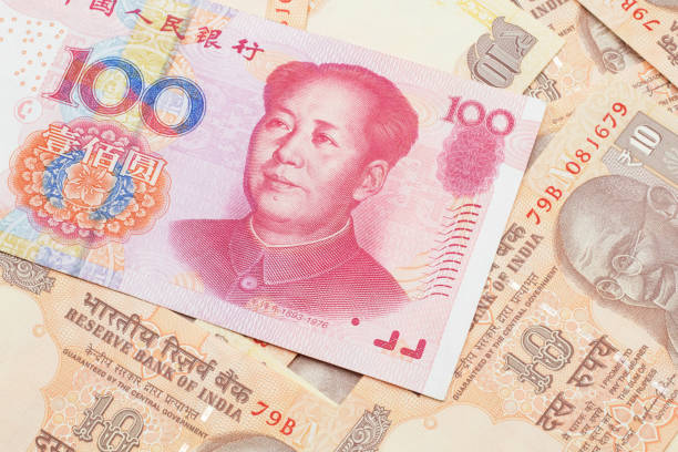 A Chinese one hundred yuan note on a background of Indian rupee bills stock photo