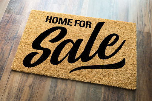 Home For Sale Welcome Mat On A Wood Floor Background.