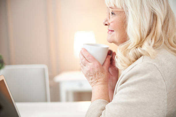 istock Happy attractive old lady enjoying hot drink at home 1205850976