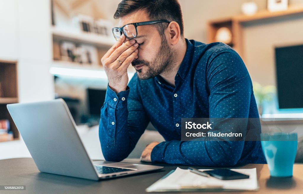Home office Tired young businessman working at home using lap top and looking Anxious Emotional Stress Stock Photo