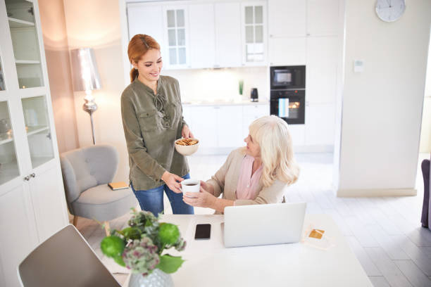 istock Happy old lady taking hot drink from female volunteer 1205854068