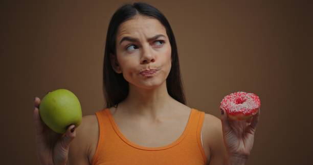 istock Seriously brunette woman choosing between apple and donut isolated on brown background 1205854928