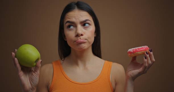 istock Seriously brunette woman choosing between apple and donut isolated on brown background 1205854935