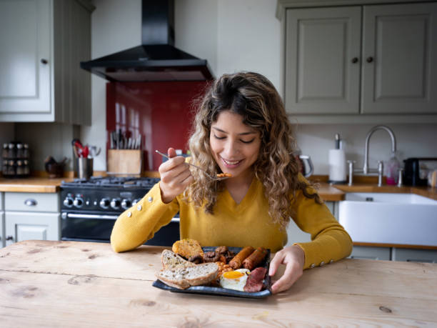 bella giovane donna a casa che si gode una deliziosa colazione inglese - breakfast eggs fried egg sausage foto e immagini stock