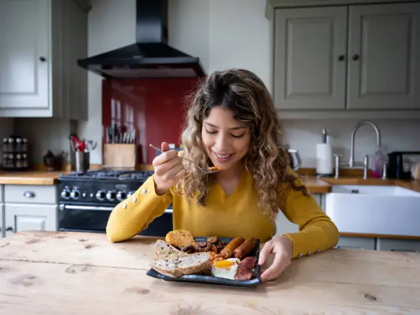 Photo of Beautiful young woman at home enjoying a delicious english breakfast