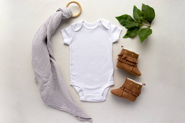 Blank gender neutral white baby bodysuit close up - with leaves and brown booties - newborn apparel mockup newborn apparel mockup gender neutral photos stock pictures, royalty-free photos & images