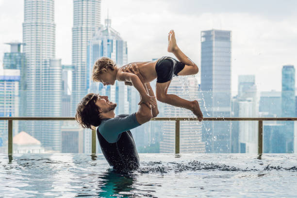 pai e filho em piscina ao ar livre com vista para a cidade no céu azul - 3670 - fotografias e filmes do acervo
