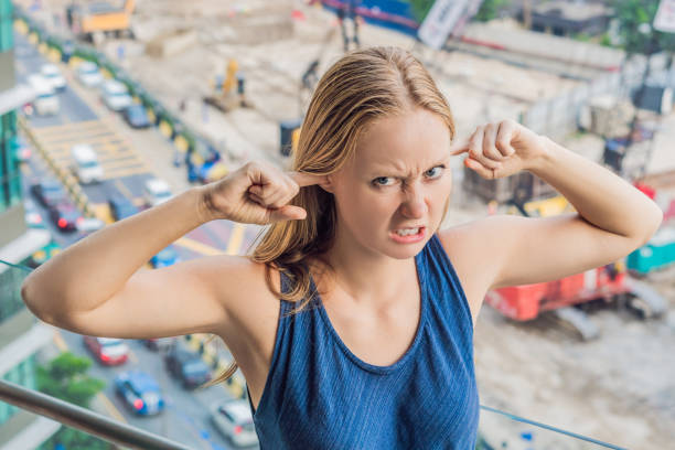 eine junge frau am fenster, die sich über das gebäude ärgert, arbeitet draußen. lärmkonzept - building activity audio stock-fotos und bilder