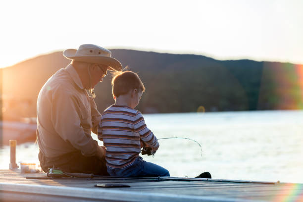 grand-père et petit-fils pêchant au coucher du soleil en été - fishing lake grandfather grandson photos et images de collection