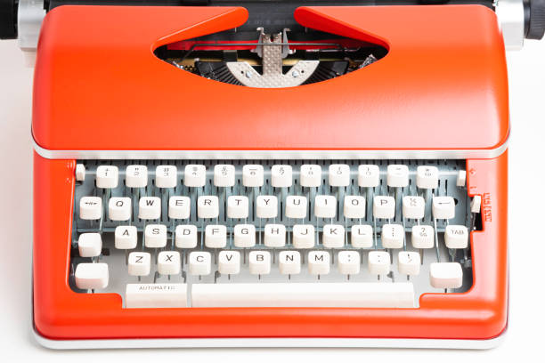 A studio shot of a retro-style portable manual typewriter with ivory-color plastic keyboard and red-orange metal casing.