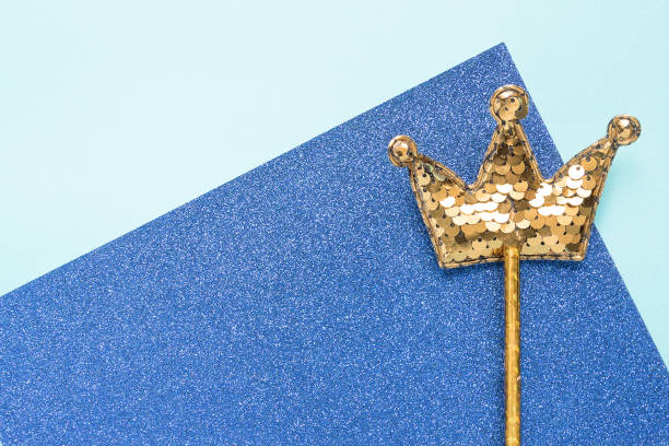 istock golden magic stick from sequins in crown shape on blue glitter background. Creative flat layclose up 1205894484