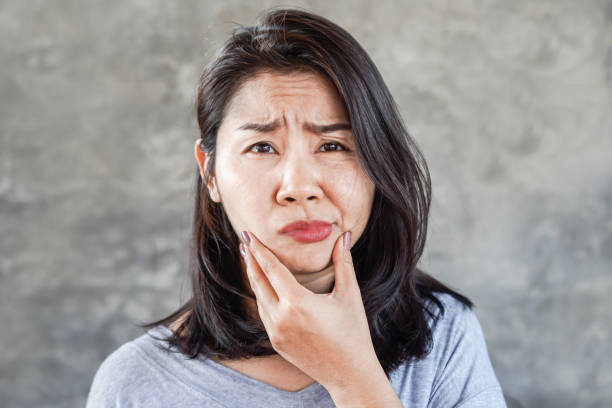 depressed asian woman having problem with bell's palsy/facial palsy, hand holding her face - serious women asian ethnicity human face imagens e fotografias de stock