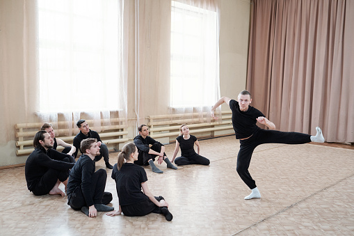 Young man wearing black outfit showing contemporary dance move to his team, horizontal shot
