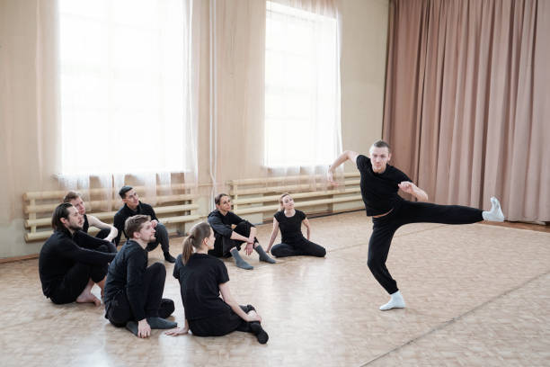 Man Showing Dance Move Young man wearing black outfit showing contemporary dance move to his team, horizontal shot contemporary dance stock pictures, royalty-free photos & images