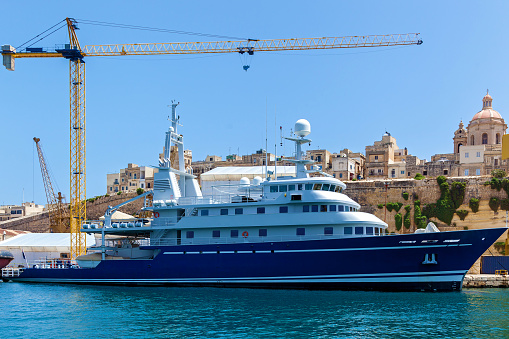 A luxury yacht moored in the port against traditional Maltese buildings.