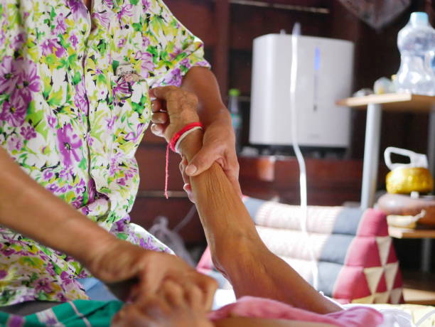 hands of a woman holding / securing an older person's arm, while giving the elderly a bed bath with a washcloth at home - wiping feet imagens e fotografias de stock