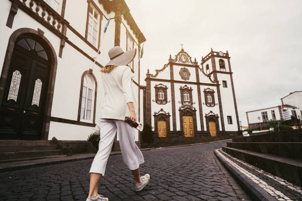 woman traveling in azores island walking in city with white buildings and clock tower - ponta delgada imagens e fotografias de stock