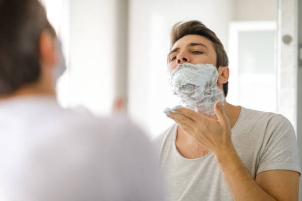 Morning bathroom routine Young man applying shaving foam on his face in the bathroom at home shaving cream stock pictures, royalty-free photos & images