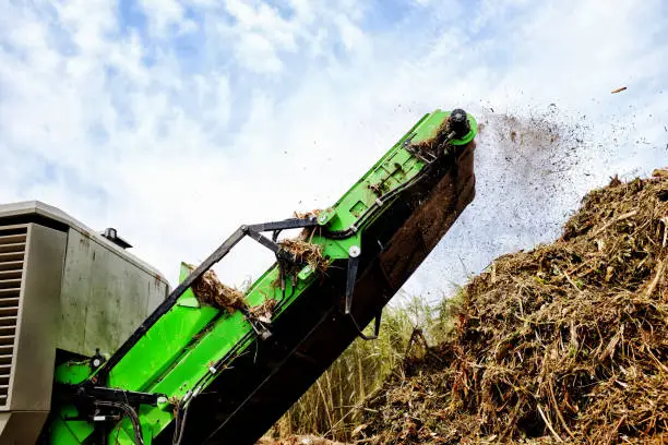 A huge green machine sprays out pulverized garden refuse onto a giant compost heap at a municipal recycling plant.
